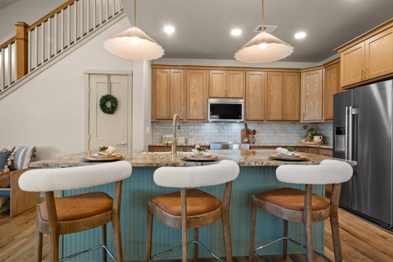 Well-lit kitchen in a Copper Creek home featuring a spacious teal kitchen island with a built-in sink. There is seating that makes it perfect for socializing or quick meals. The kitchen includes modern appliances such as a microwave and fridge.